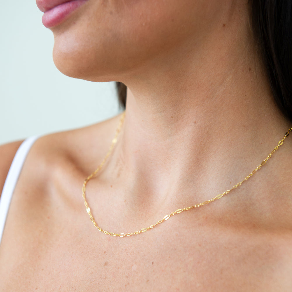 Gold glimmer chain necklace on a woman against a light background