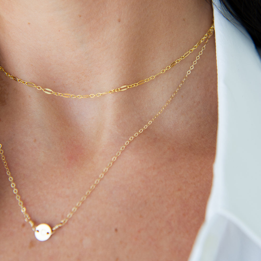 Gold glimmer chain necklace layered with a personalized necklace on a woman's neck