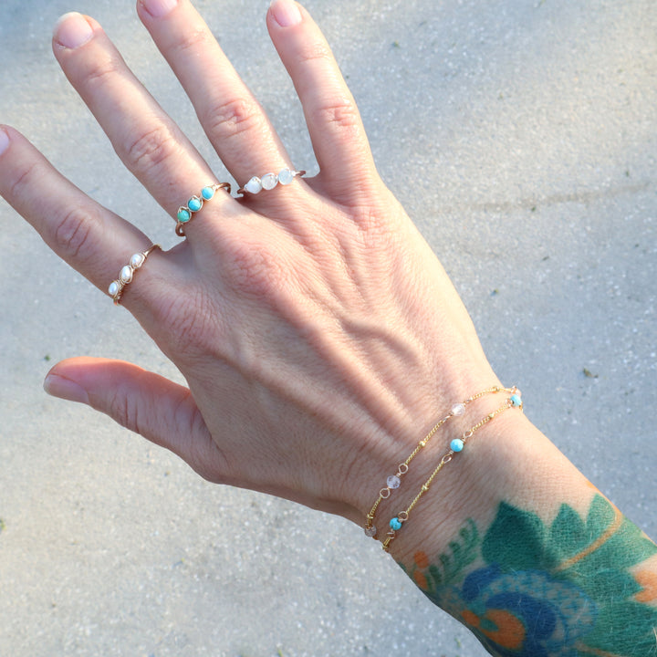 Hand wearing birthstone bracelet in 14k gold filled with quarts and turquoise gemstones and birthstone ring sin sterling silver and 14k gold filled with aquamarine, turquoise and pearl gemstones