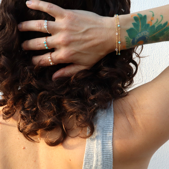 hand wearing birthstone rings and matching birthstone bracelets in turquoise, quartz, aquamarine and pearl
