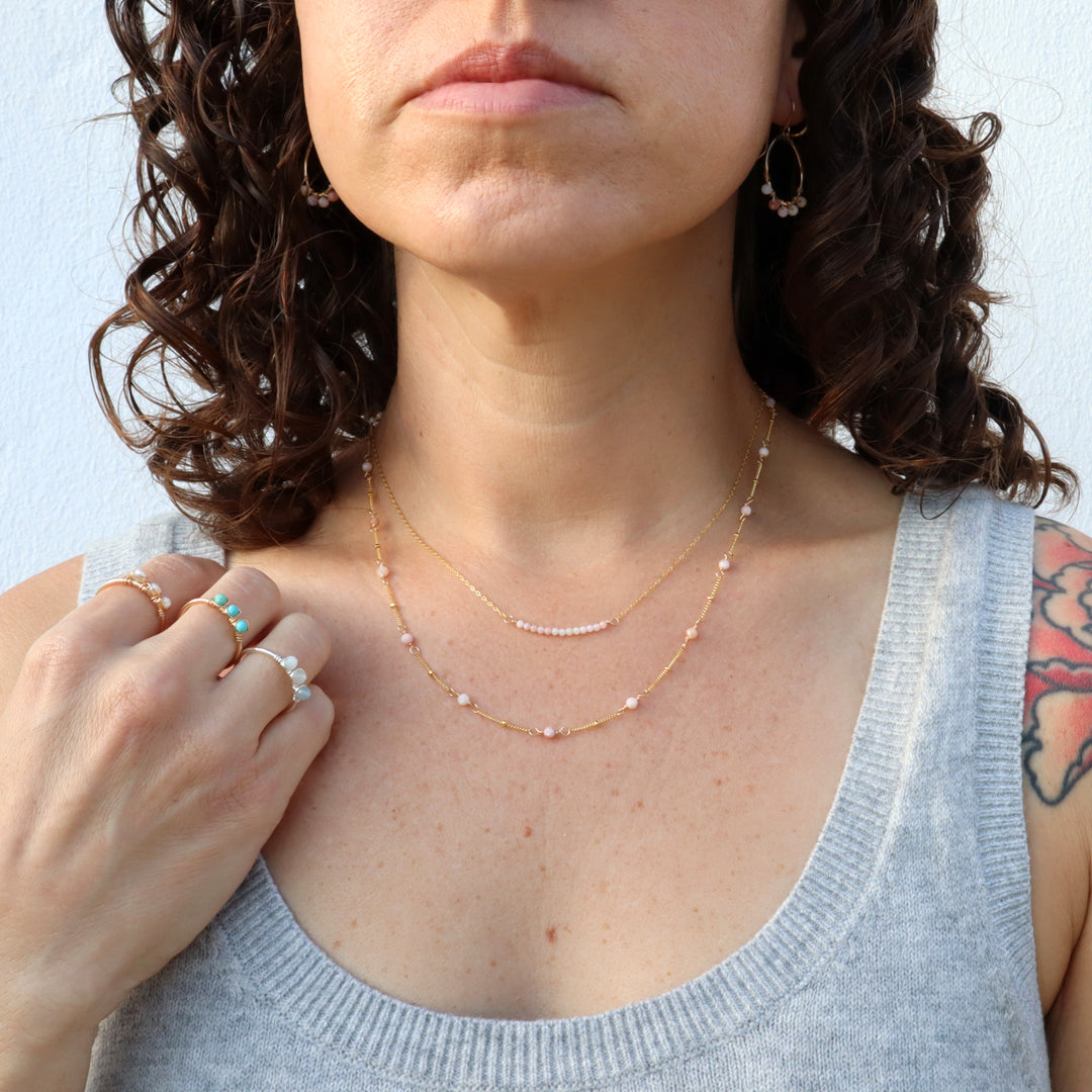 model wearing birthstone necklace and birthstone earrings with pink opal gemstones and birthstone rings with pearls, turquoise, aquamarine