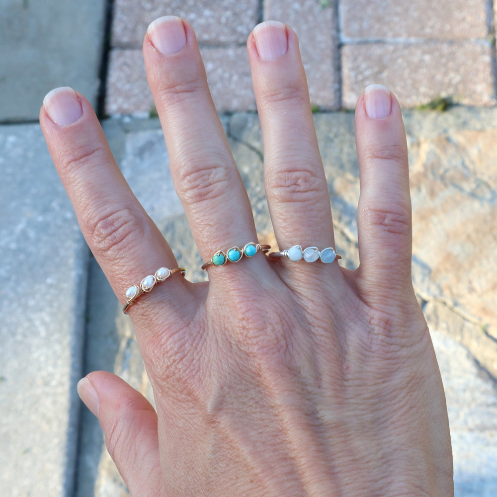 hand wearing birthstone rings in pearl, turquoise and aquamarine