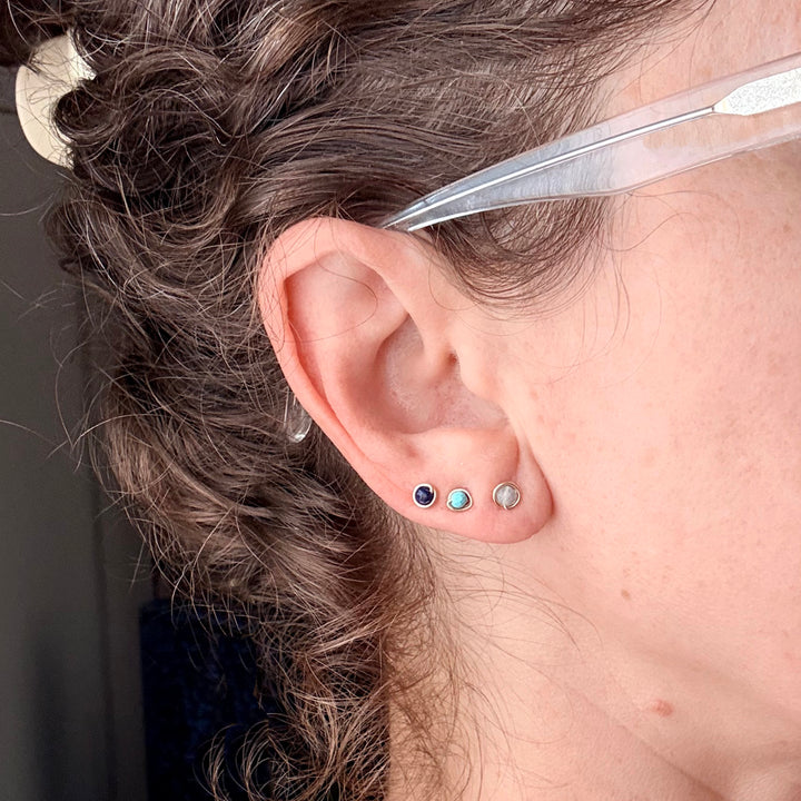 close up of an ear with birthstone stud earrings in 14k gold filled with aquamarine, turquoise and lapis faceted gemstones