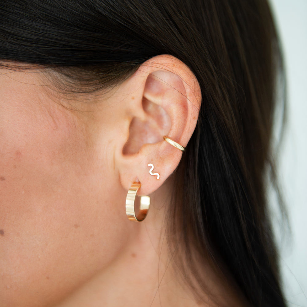 Close-up of an ear wearing gold bold hoop earrings a squiggle stud and an ear cuff