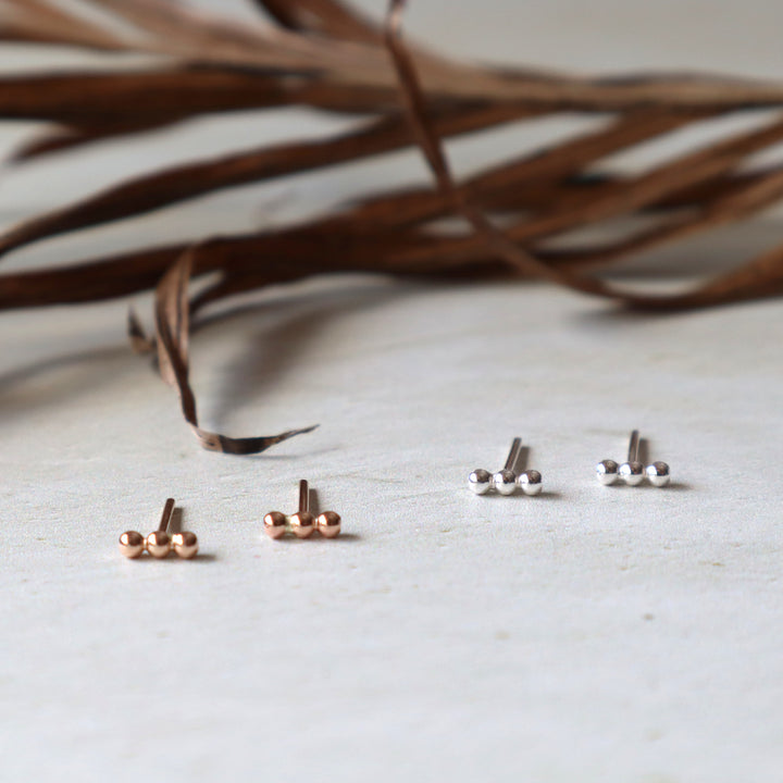 Set of small gold and silver beaded stud earrings on a light surface with dried leaves in the background.