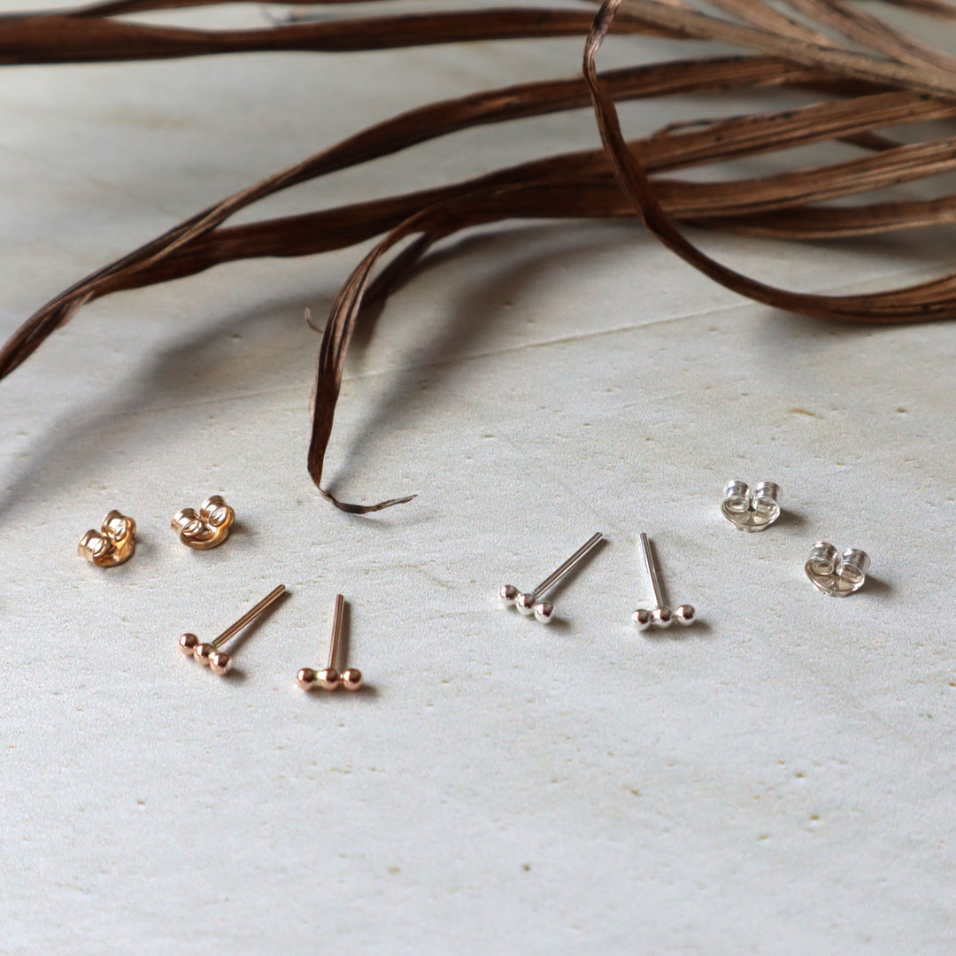 Collection of gold and silver beaded stud earrings on a light surface with dried leaves.