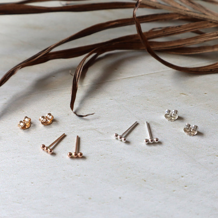 Collection of gold and silver beaded stud earrings on a light surface with dried leaves.