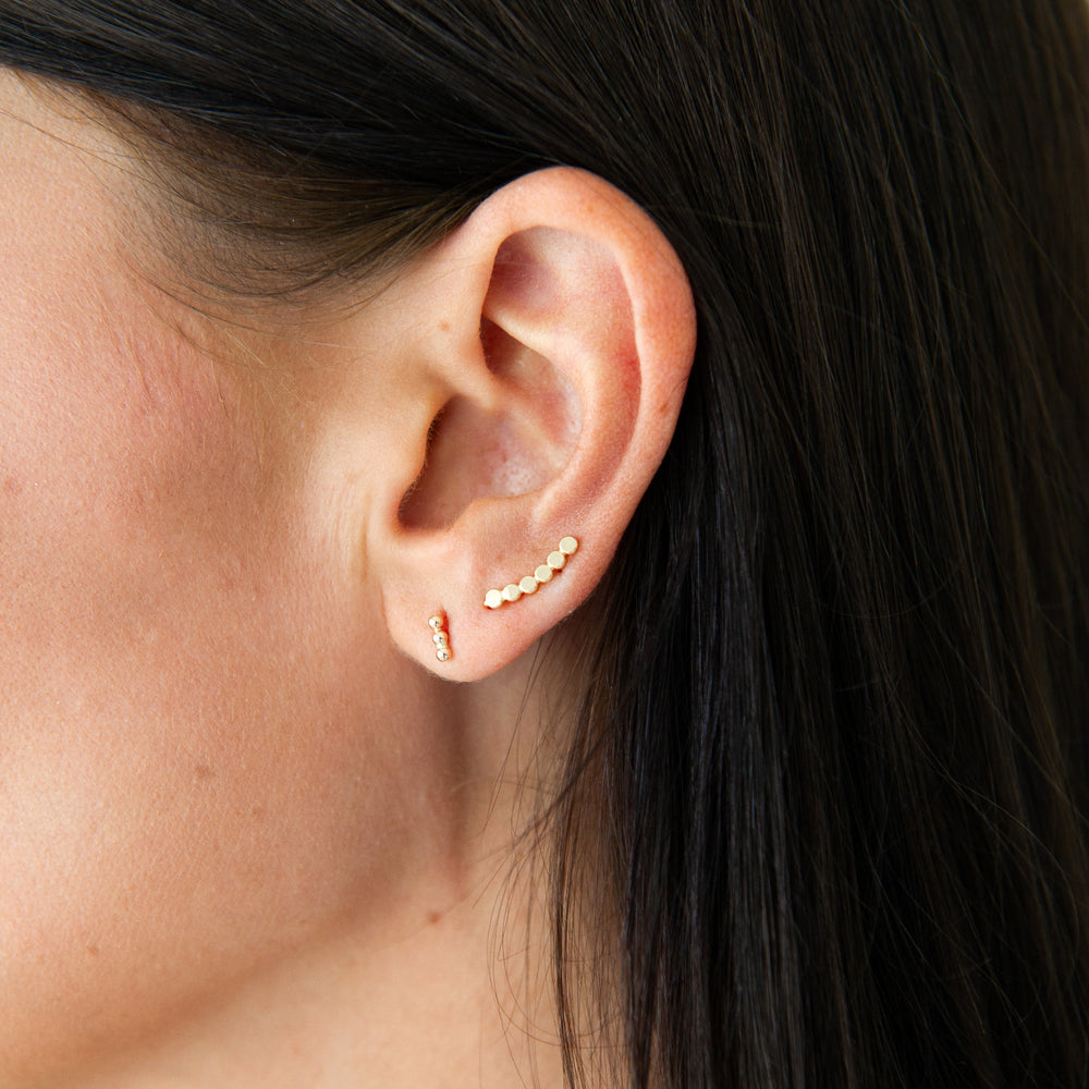 Close-up of an ear with gold beaded stud earrings and a beaded mini ear climbr
